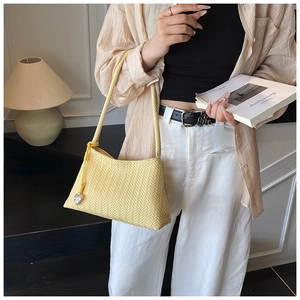 Close-up of bright yellow woven hobo bag with herringbone texture and heart charm