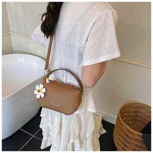 Brown lychee leather crossbody bag styled with a daisy charm in a cozy home setting