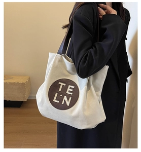 Detail of canvas tote bag with brown leather strap and circular TE LN logo patch