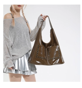 Detail of dark brown glossy leather tote bag featuring metal rivets and front pockets