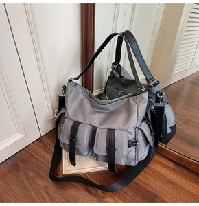 Detail of grey nylon tote bag showing flap buckle pockets on a minimalist wood floor