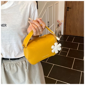 Detail of yellow lychee texture leather handbag with white flower charm and tassel accessory