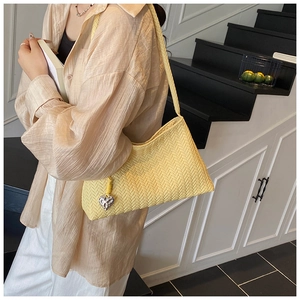 Detail of a bright yellow woven hobo bag with an elegant heart-shaped silver charm