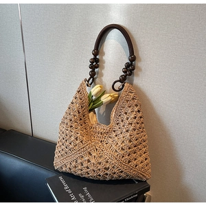 Detail of woven straw tote bag featuring intricate hollow patterns and brown beaded handles
