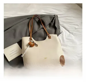 Close-up of beige lychee grain leather tote bag with brown trim and cute bear charm