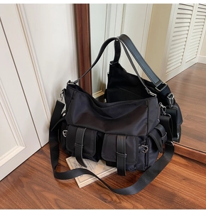 Detail of black nylon tote bag showing multi-pocket structure and leather buckles