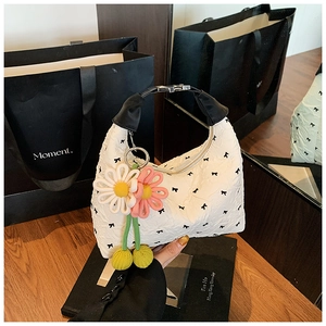 Detail der weißen Plissee-Tasche mit schwarzen Schleifen und buntem Blumenanhänger