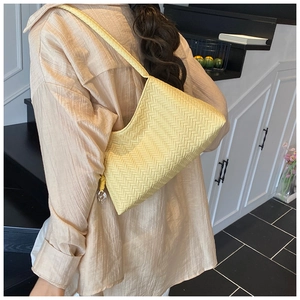 Detail of light yellow woven handbag featuring herringbone texture and heart pendant