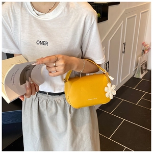 Close-up of yellow lychee grain handbag with flower charm held by a model