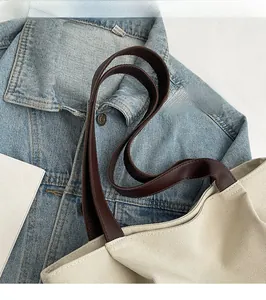 Detail view of smooth dark brown leather long shoulder strap on cream canvas tote bag
