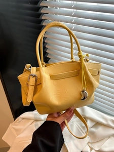 Yellow textured leather bucket bag with top handles and silver pendant in soft natural light