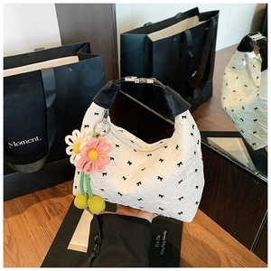 Detail einer weißen Handtasche mit gerafftem Stoff, Schleifenmuster und Blumenanhänger