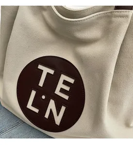 Detail of the cream canvas tote bag with a brown round leather patch and logo embroidery