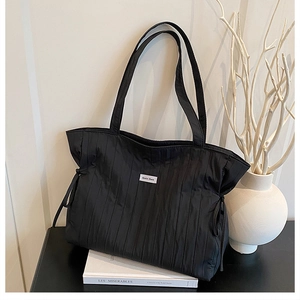 Dettaglio della borsa tote nera con pieghe sottili, texture a coulisse e stile minimalista