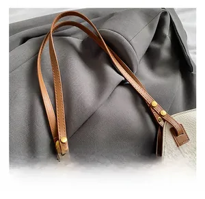 Detail showing off-white lychee leather texture and brown strap with gold rivets