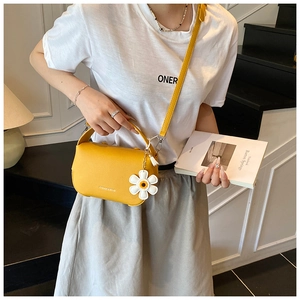 Detail of yellow lychee texture handbag with daisy pendant and fashion text branding