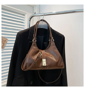 Détail du sac sous le bras en cuir marron brillant avec boucle dorée et deux poignées