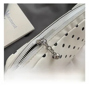 Detailed close-up of a white polka dot bag with a silver metal zipper and chain pull