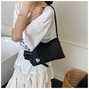Detail of black woven shoulder bag featuring a silver heart pendant and textured pattern