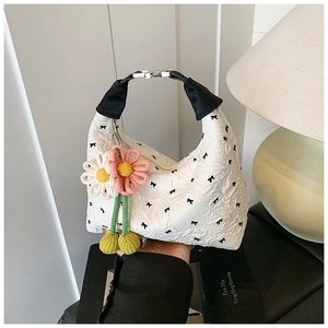 Nahaufnahme einer weißen Faltenhandtasche mit Schleifenmuster und Blumenanhänger