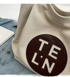 Close-up of cream canvas tote bag with round leather logo patch and casual denim style
