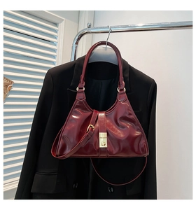 Détail macro du sac à bandoulière en cuir verni bordeaux avec boucle dorée