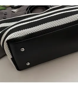 Détail des pieds en métal argenté sur le sac fourre-tout tissé à rayures noires