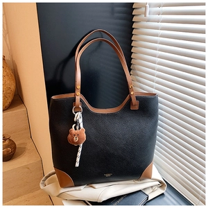 Detail of black pebbled leather tote bag with brown straps and cute bear pendant charm