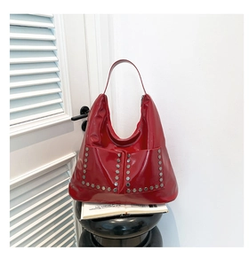 Close-up of red high-shine leather hobo bag featuring silver hexagonal rivets and dual pockets