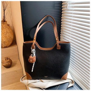 Close-up of black pebble leather tote bag with brown accents and a cute bear charm