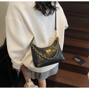 Sac bandoulière matelassé noir avec chaîne dorée et fermoir rotatif porté par un mannequin