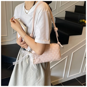 Detail of pink polka dot handbag featuring lace bow and pearl charm accessories