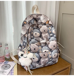 Detail of grey school backpack featuring cute animal prints and a white plush pompom charm