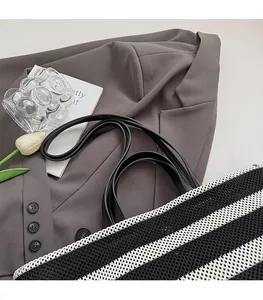 Détail du sac cabas tissé à rayures noires et blanches avec anses en cuir sur un veston