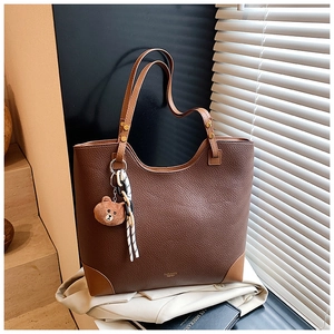 Detail of dark brown pebble leather tote bag with plush bear charm and reinforced corners