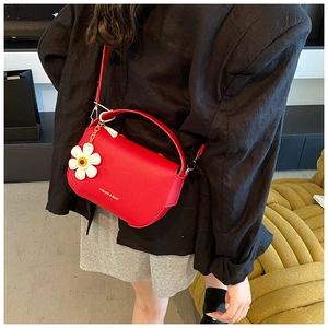 Close-up of red lychee texture handbag featuring a white daisy charm and gold lettering