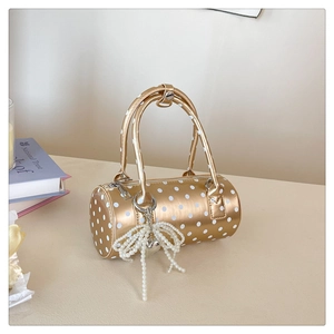 Détail du sac cylindre doré à pois avec breloque nœud en perles et fermeture zippée