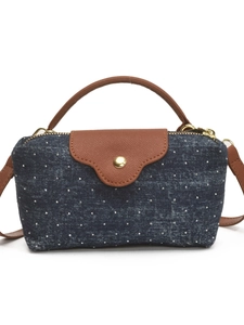 Navy blue polka dot denim crossbody bag with brown leather handle on white background
