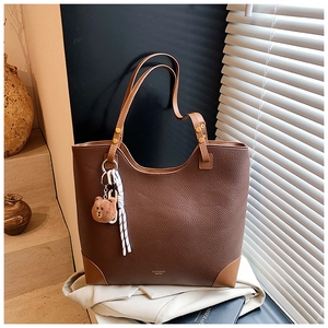 Close-up of brown lychee grain tote bag with plush bear charm and reinforced corner details