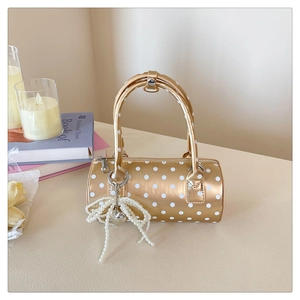 Détail du sac à main cylindrique doré à pois blancs avec pendentif nœud en perles élégant
