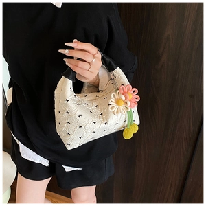 Details der weißen Plissee-Handtasche mit schwarzen Schleifenprints und Blumenanhänger