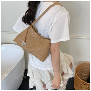 Detail of a brown woven shoulder bag featuring a silver heart pendant and rope handles