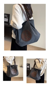 Detail of grey canvas tote bag featuring brown leather straps and a logo-engraved patch