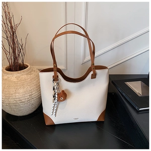 Detailed macro view of large cream tote bag with brown leather accents and bear pendant