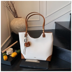 Detail of white lychee texture tote bag with brown leather trim and bear charm