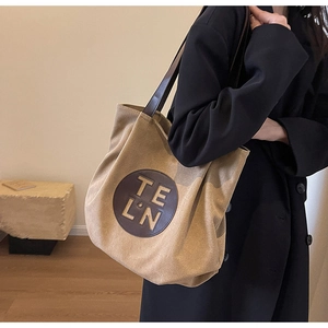 Detail of khaki canvas tote bag with round leather logo patch on a female model