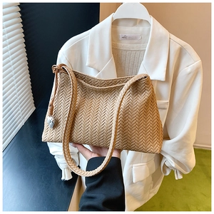 Detail of light khaki woven shoulder bag featuring a silver heart charm and textured pattern