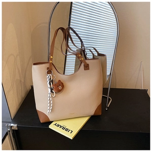 Detail of beige tote bag featuring brown leather trim and a cute plush bear charm