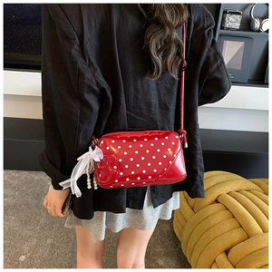 Détail du sac bandoulière rouge à pois en cuir verni avec nœud en dentelle et perle