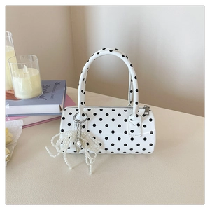 Gros plan du sac cylindre blanc à pois avec breloque nœud perlé sur fond épuré